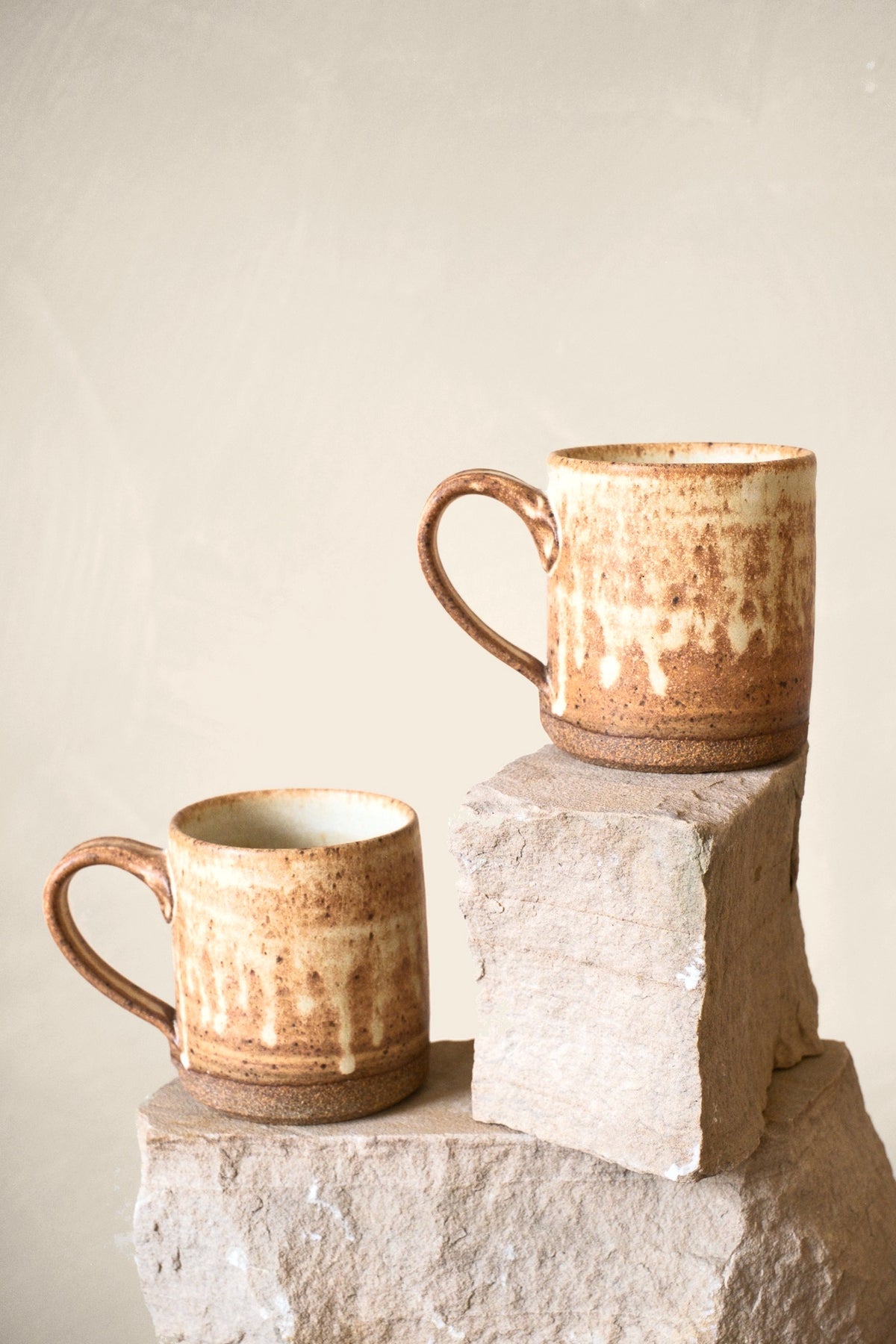 Two Liam Grinton cream drip-glaze mugs on stone